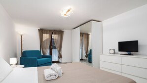 Et moderne hotelværelse med en stor seng, en blå lænestol, et fladskærms-tv og et spejl på væggen.