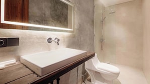 Un baño moderno con un lavamanos rectangular grande, una encimera de madera, un inodoro blanco y una zona de ducha con mampara de vidrio.