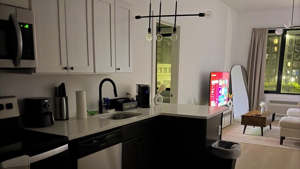 A modern kitchen with white cabinets, a built-in oven, a coffee maker, and a large window. - Cozy 2BR/2BA Retreat 5 Min from EWR, 15 Min to NYC (Elizabeth)