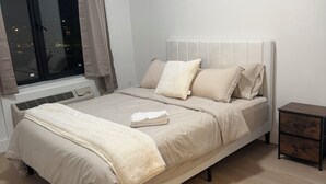 A neatly made bed with a headboard, a bedside table with drawers, and a window with curtains. - Cozy 2BR/2BA Retreat 5 Min from EWR, 15 Min to NYC (Elizabeth)