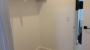 A room with a wooden floor, white walls, and a closet with open shelves and a hanging rod. - Cozy 2BR/2BA Retreat 5 Min from EWR, 15 Min to NYC (Elizabeth)