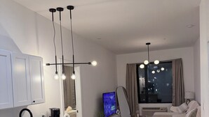 A modern kitchen with a central island, a dining area with a sofa and coffee table, and a TV in the background. - Cozy 2BR/2BA Retreat 5 Min from EWR, 15 Min to NYC (Elizabeth)