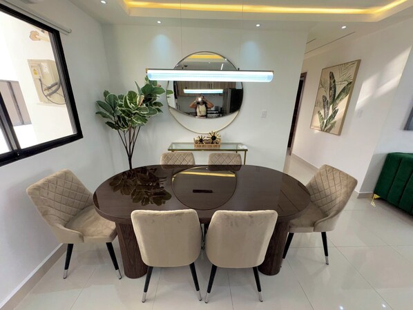 Un comedor moderno con una mesa redonda, seis sillas, un espejo grande y una planta en maceta.