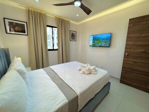 Habitación de hotel con cama, cortinas, ventilador de techo, televisor y puerta de madera.