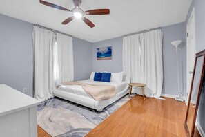 Une chambre à coucher avec un lit, un ventilateur de plafond, un tableau et une lampe sur pied.