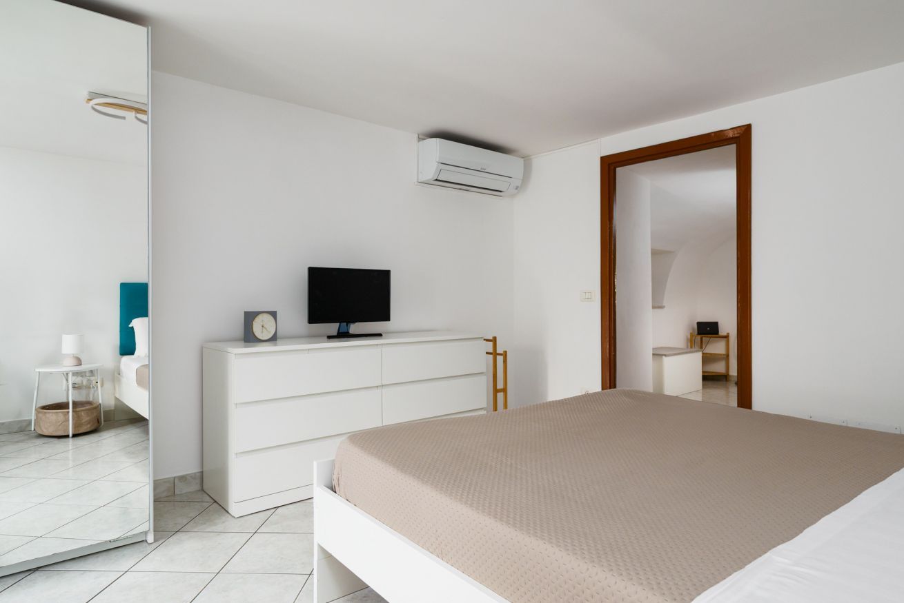 Een moderne slaapkamer met een bed, een televisie op een dressoir, een airconditioning en een spiegel.