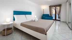 Habitación de hotel moderna con una cama grande, una mesita de noche con lámpara, una silla y vistas al exterior.