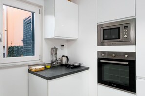 Una cocina con ventana, microondas, tostadora y tetera.