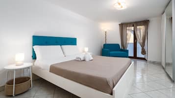 Una camera d'albergo moderna con un letto grande, un comodino con una lampada, una sedia e vista all'esterno.