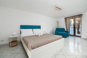 Un dormitorio con cama, una silla, una lámpara y una ventana con cortinas.