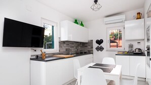 Una cocina moderna con armarios blancos, un televisor negro y una zona de comedor con sillas blancas.