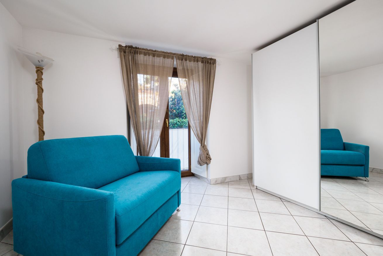 A room with a blue sofa, a large mirror, and a view through a window with curtains.