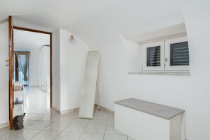 Un pasillo con una puerta que da a una habitación, un espejo grande apoyado en la pared y un ventanal pequeño con persianas.