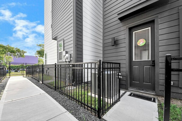 A modern building with a black door and a window with a sticker. There is a black metal fence and a concrete pathway leading to the entrance.