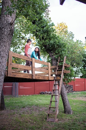 A wooden platform with a ladder, surrounded by trees and a red fence.