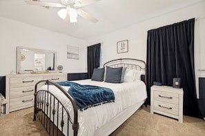 A bedroom with a bed, a nightstand, a dresser, a ceiling fan, and a wall-mounted clock.