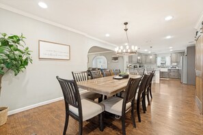 A spacious dining area with a large wooden table and chairs, a chandelier, and a potted plant.