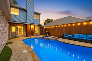 A backyard with a swimming pool, a barbecue area, and a seating area with blue cushions.
