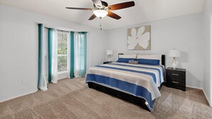A bedroom with a bed, a ceiling fan, a nightstand, and a window with curtains. - Modern 5BR/2.5BA w/Private Pool  Sleeps 16 ppl (Allen)