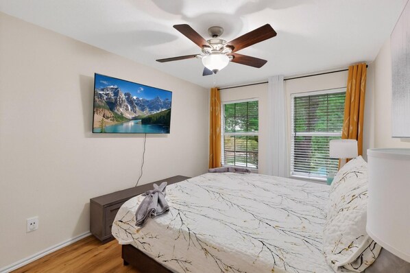 A bedroom with a bed, a ceiling fan, a window with curtains, and a painting on the wall.