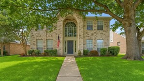 A two-story building with a central arched entrance, a flag, and a well-maintained lawn. - Modern 5BR/2.5BA w/Private Pool  Sleeps 16 ppl (Allen)