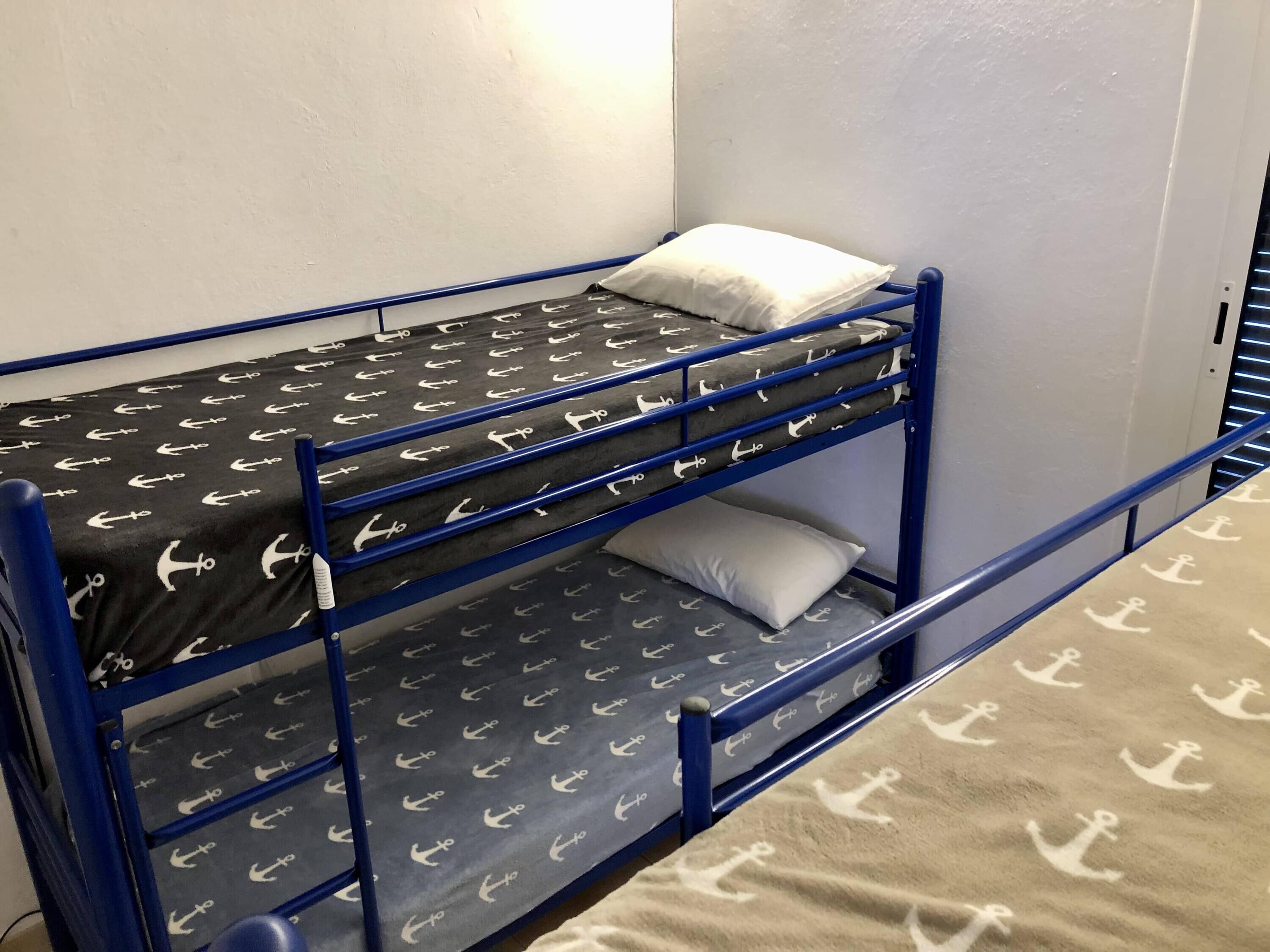 A bunk bed with a black and white anchor pattern, a white pillow, and a blue metal frame.