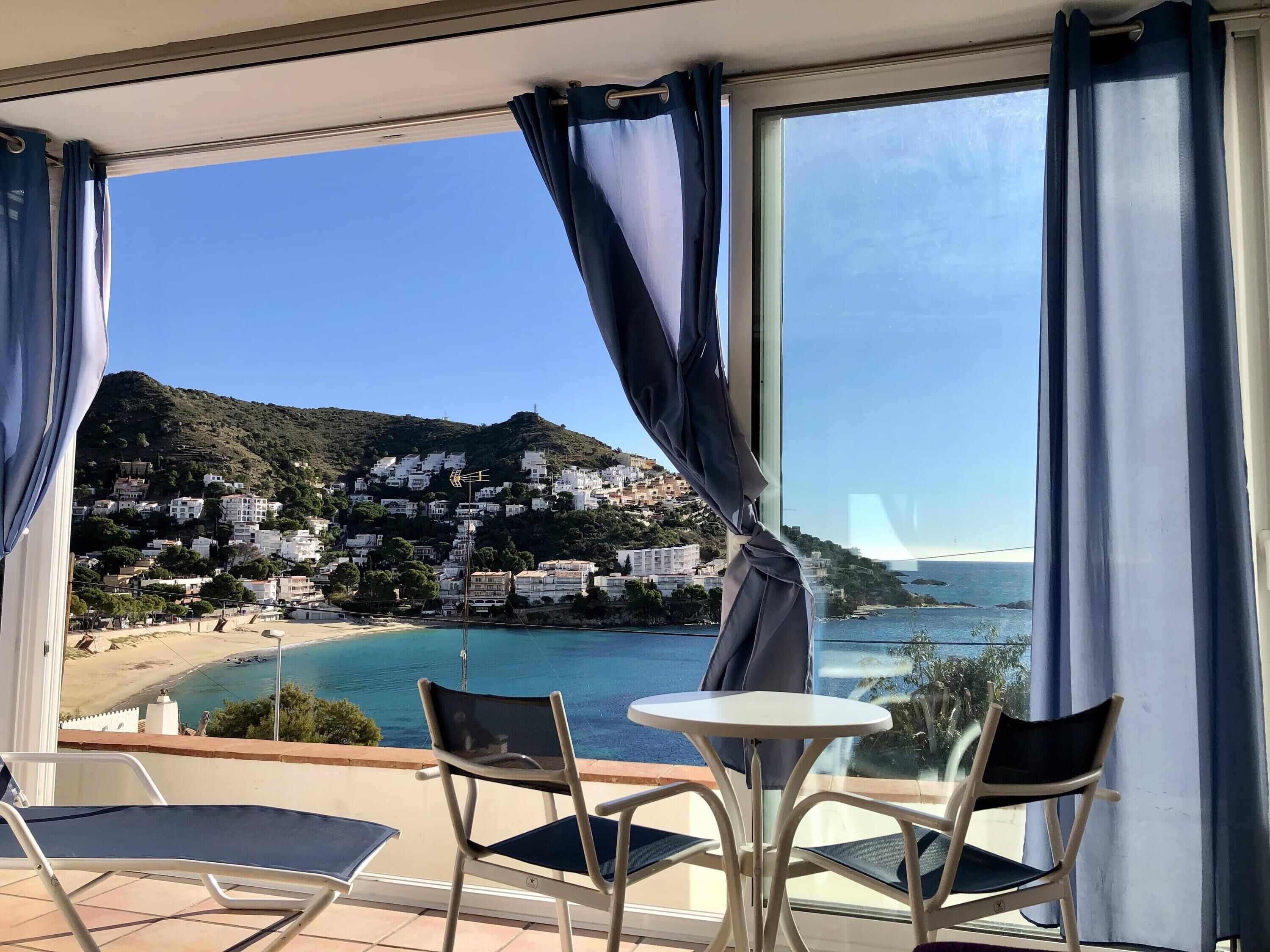 Un balcone con tavolo e sedie, con vista su una zona costiera con edifici su una collina e una spiaggia.
