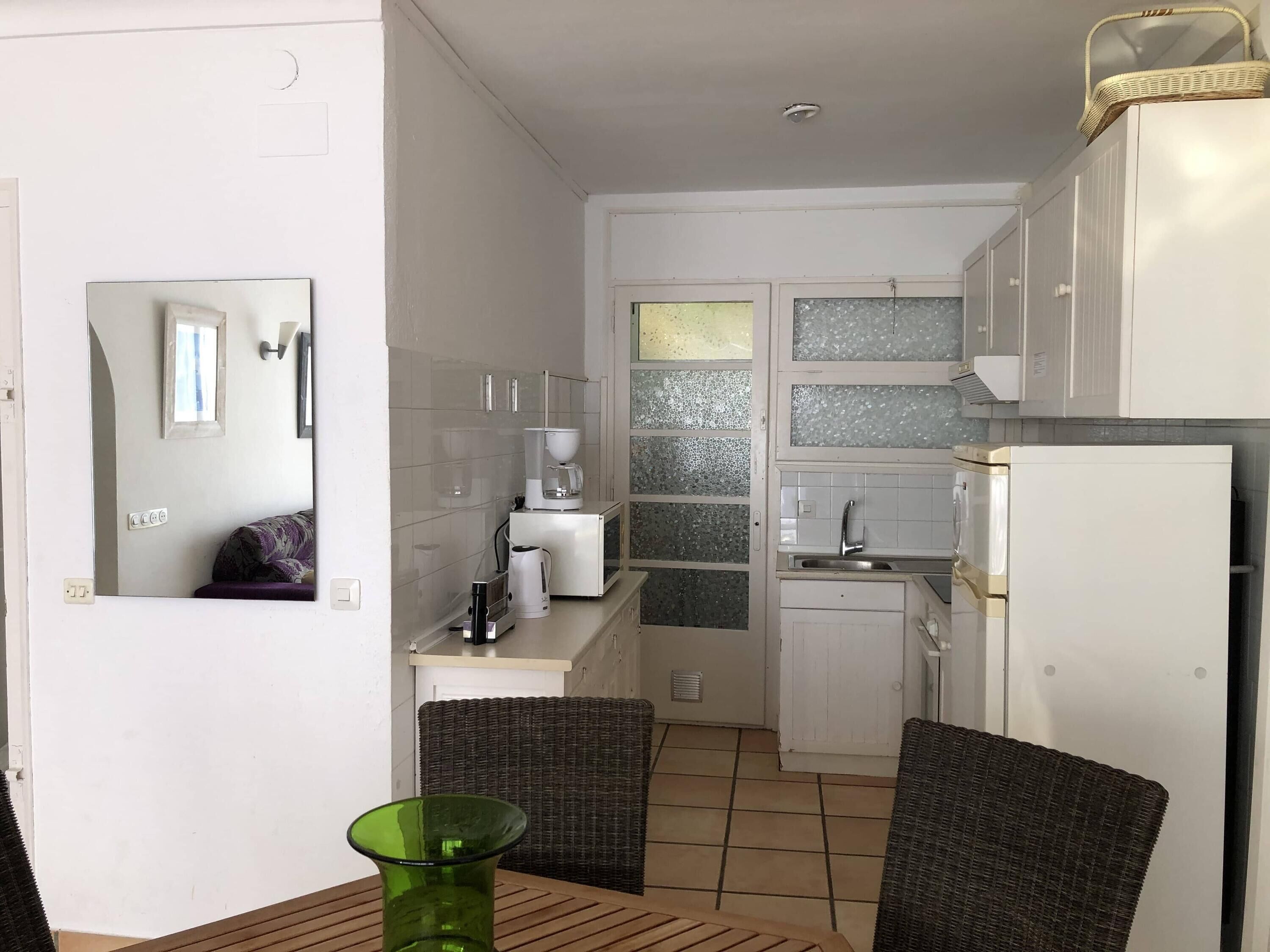Una cocina compacta con armarios blancos, una cafetera y un refrigerador.