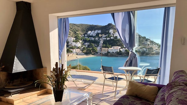 A living room with a large window overlooking a coastal town, a fireplace, and a seating area with a sofa and chairs. - Apartment in Roses on the seafront.MONTEMAR (Roses)