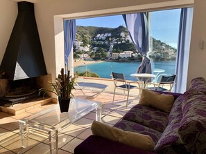A living room with a large window overlooking a coastal town, a fireplace, and a seating area with a sofa and chairs. - Apartment in Roses on the seafront.MONTEMAR (Roses)
