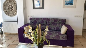 A living room with a purple sofa, a glass coffee table, and a vase with flowers. There are two framed pictures on the wall and a decorative wall hanging. - Apartment in Roses on the seafront.MONTEMAR (Roses)