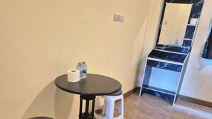 Una habitación pequeña con una mesa redonda, dos taburetes blancos, un espejo y un dispensador de agua.