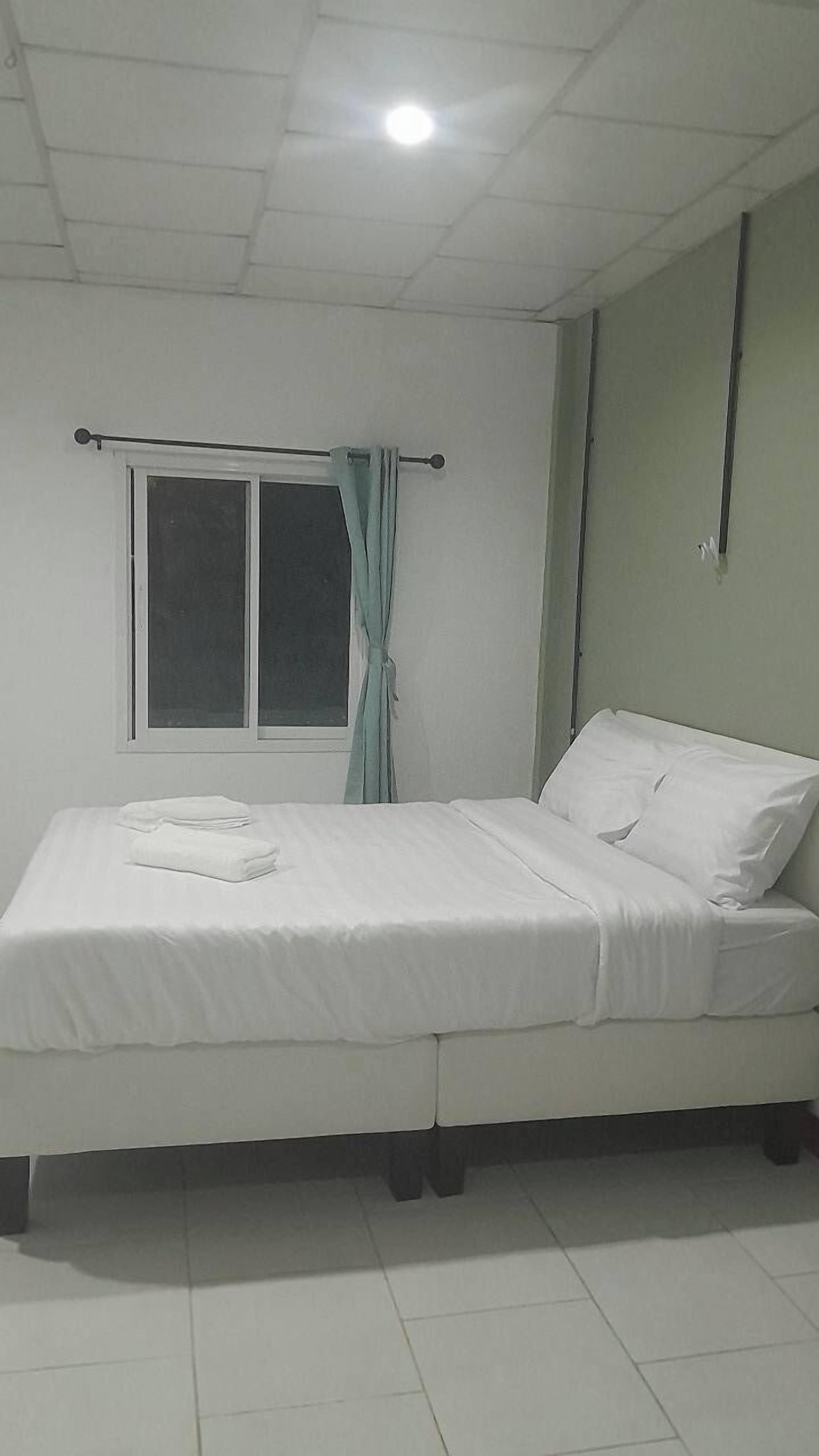 A single-bed room with a window, a curtain, and a bed with white bedding.