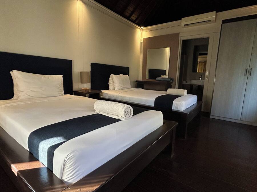 A hotel room with two beds, a wardrobe, a mirror, and a bedside table with a lamp.