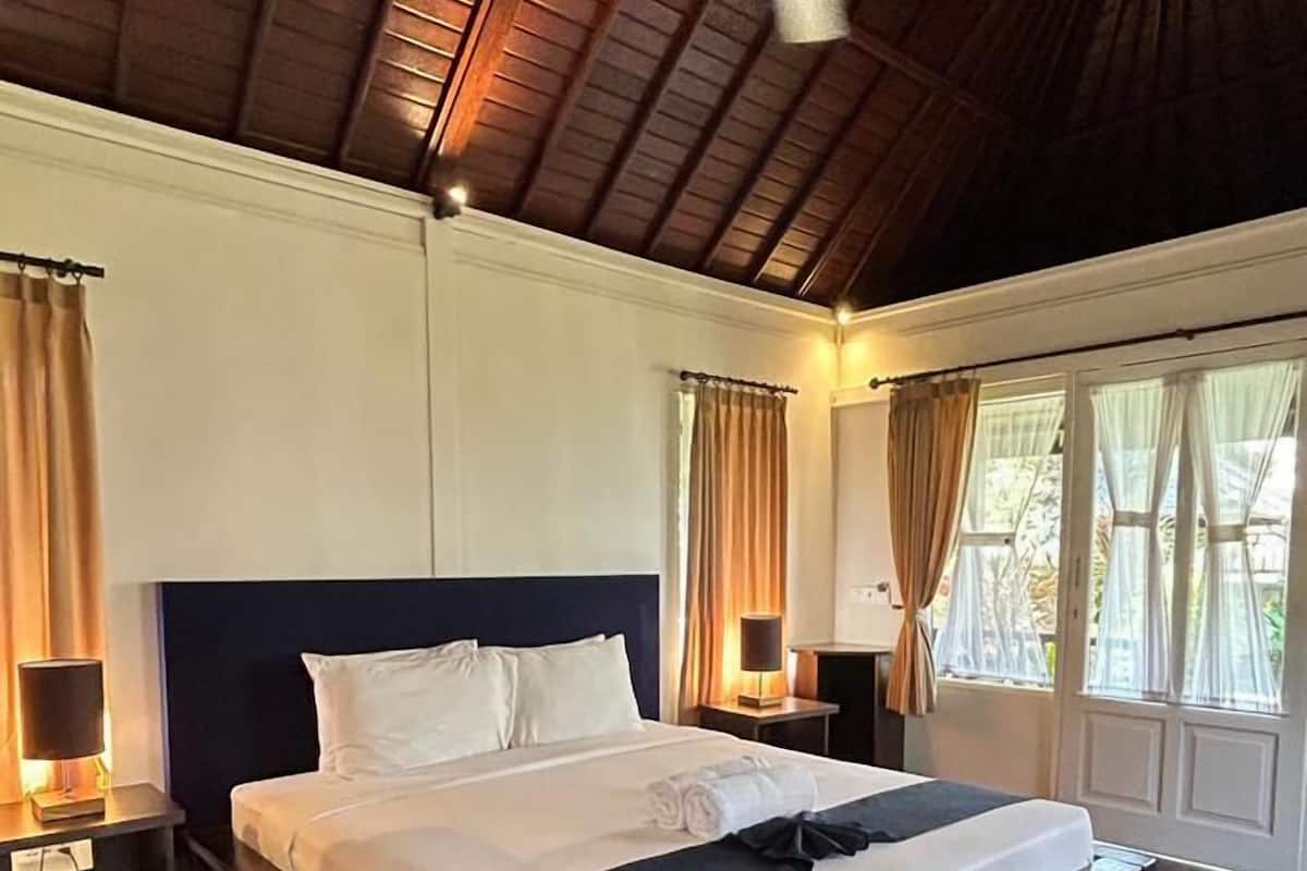 A spacious bedroom with a large bed, wooden ceiling, and a ceiling fan.