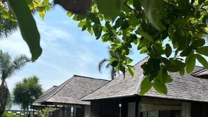 A bungalow with a thatched roof, surrounded by a well-maintained lawn and tropical plants. - Balangan Surf Resort (Jimbaran)