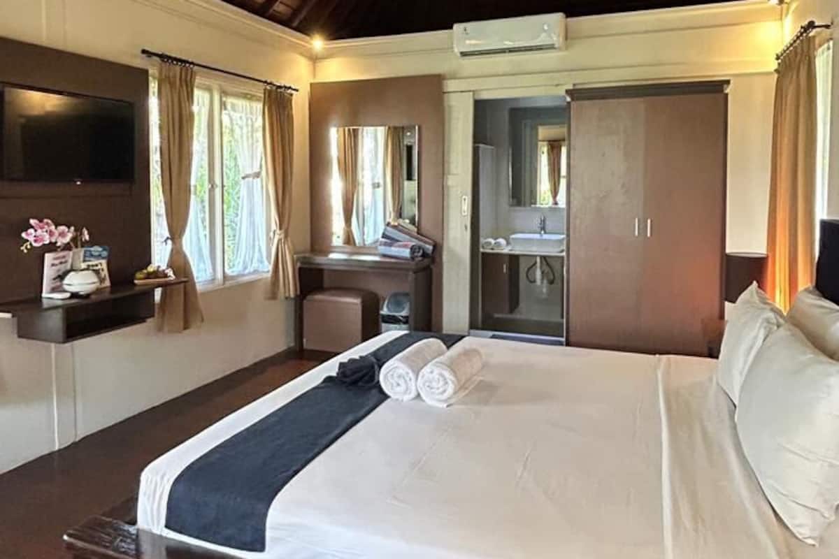 A bedroom with a large bed, a ceiling fan, a desk with a chair, a mirror, and a wardrobe.