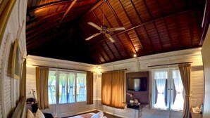A spacious bedroom with a large bed, a ceiling fan, and a TV on a stand. - Balangan Surf Resort (Jimbaran)