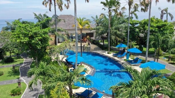A resort with a large swimming pool, lounge chairs, and palm trees. - Balangan Surf Resort (Jimbaran)