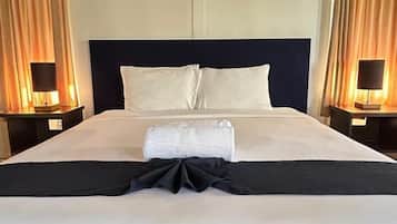 A hotel room with a large bed, two bedside tables, a headboard, and curtains.