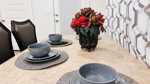 Una mesa de comedor con platos y tazones, un florero con flores, y una pared con diseño.