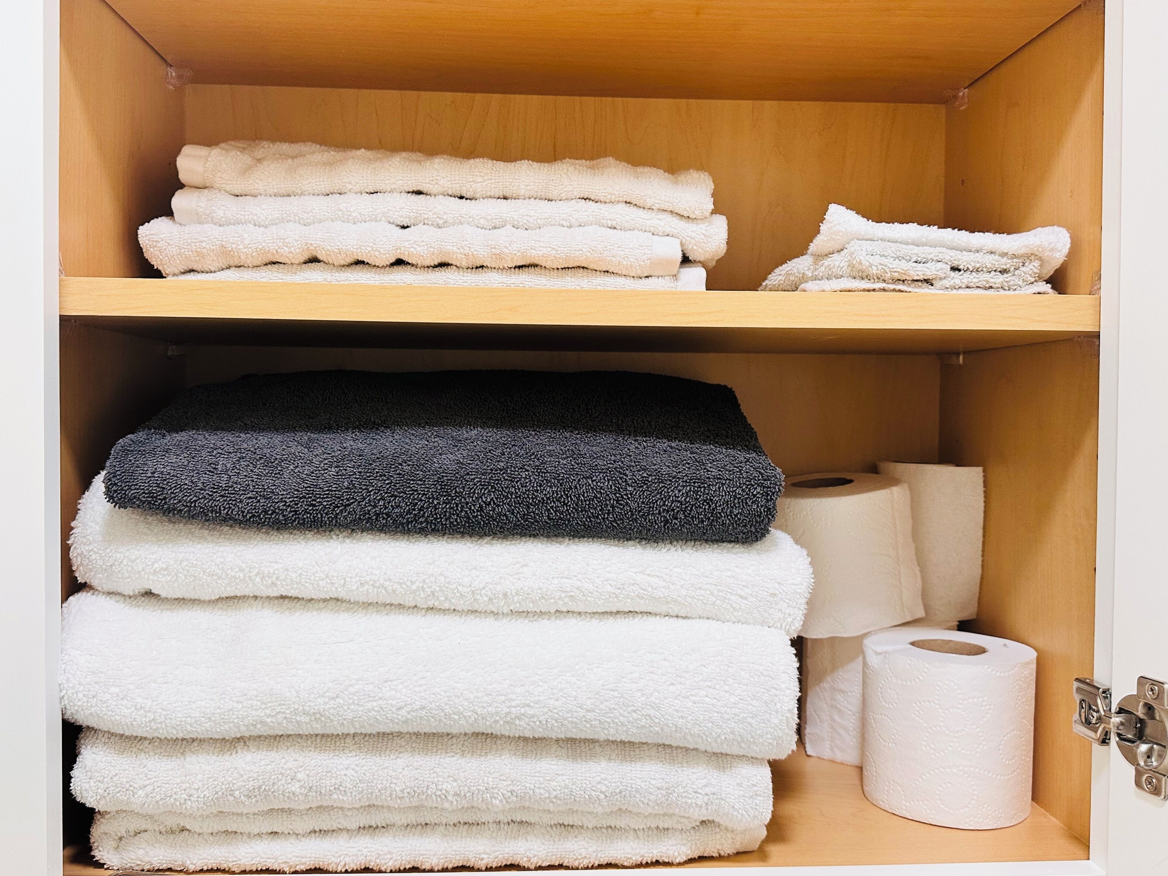 A wooden cabinet with shelves holding folded towels and a roll of toilet paper.
