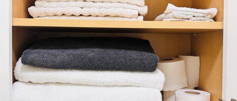 A wooden cabinet with shelves holding folded towels and a roll of toilet paper.