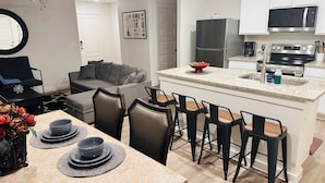 Una cocina moderna con una isla central, taburetes de bar y un comedor con una mesa dispuesta para cuatro.