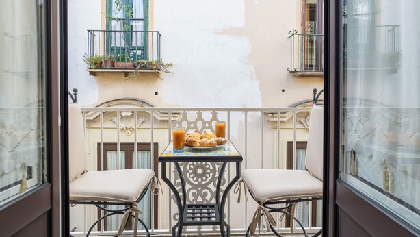 Un balcon avec deux chaises, une table sur laquelle se trouve une assiette de nourriture et des boissons, et des plantes en pot posées sur la rambarde.