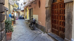 Une ruelle étroite pavée de pierres, avec une moto garée sur le bord, une porte en bois et une enseigne indiquant une boutique de produits en cuir.