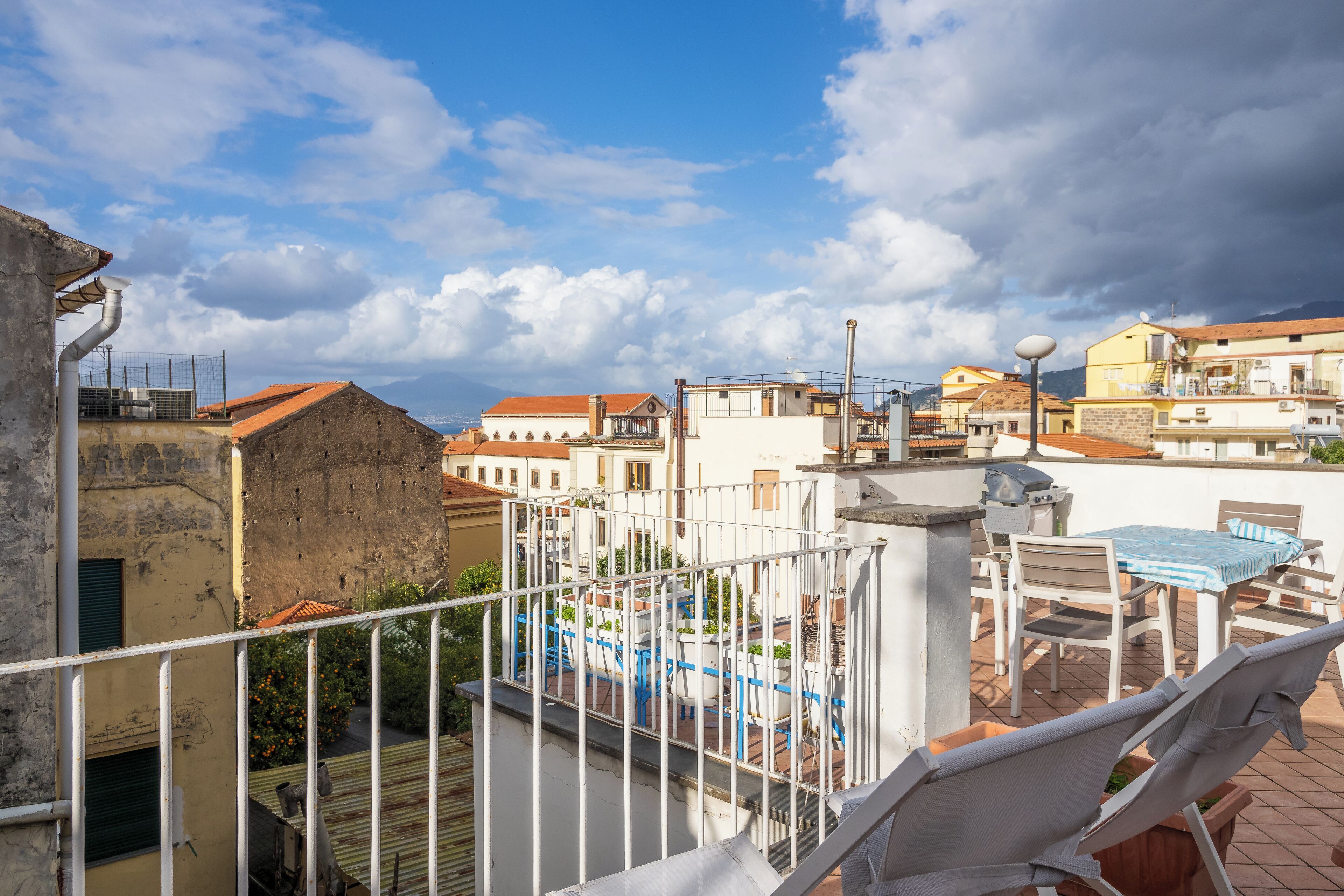 A rooftop terrace with a table and chairs, a railing, and a view of the cityscape.