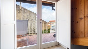 Une pièce dotée d’une porte-fenêtre coulissante donnant sur un balcon, avec un tableau blanc, un sol carrelé et une vue sur des immeubles et une colline.