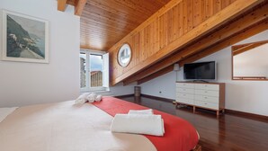 Une chambre dotée d’un grand lit, de poutres apparentes en bois au plafond, d’une télévision et d’une fenêtre donnant sur l’extérieur.