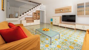 Un salon moderne avec un escalier, un téléviseur et une table basse sur laquelle sont disposés des fruits.